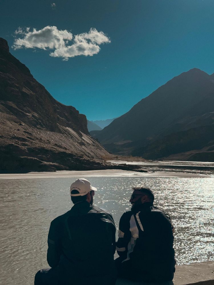 Two riders resting by a river in the Ladakh mountains